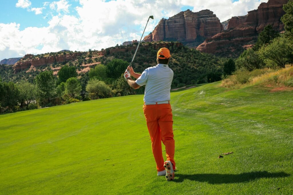 Golfer swinging on a picturesque hillside golf course with vibrant landscape.